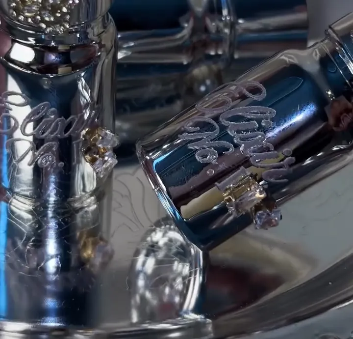 Two chrome Perfume Elixir dropper bottles with engraved script and crystal charms, resting on a mirrored tray.